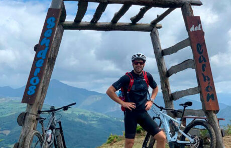 Un ciclista parado en frente de un arco de madera que pone Flow Trail, se ven dos bicicletas